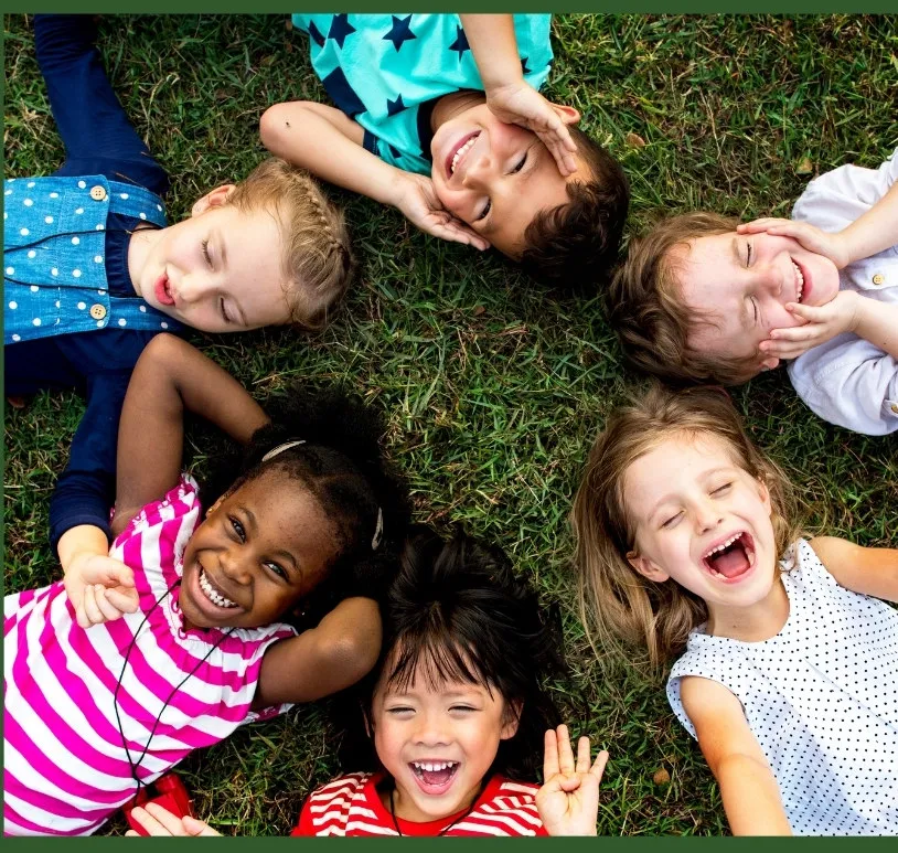 Six children lying in a circle on the grass, laughing together